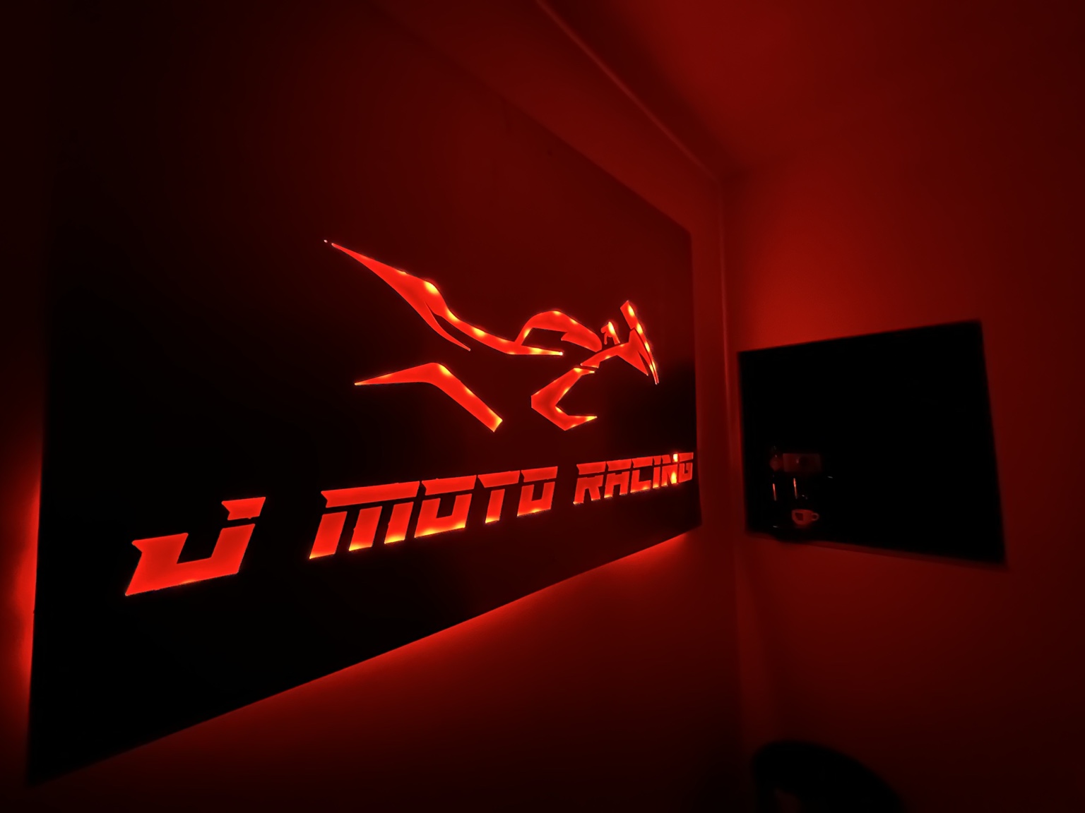 Enseigne lumineuse rouge J-Moto Racing dans l’atelier